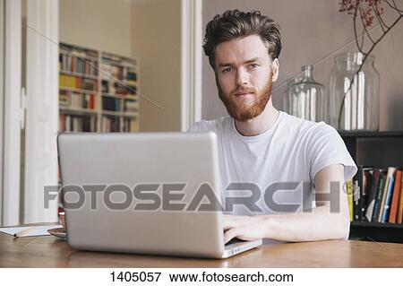 Portrait of confident young man using laptop at table View Large Photo Image Stock Photo - Portrait of confident young man using laptop at table. Fotosearch