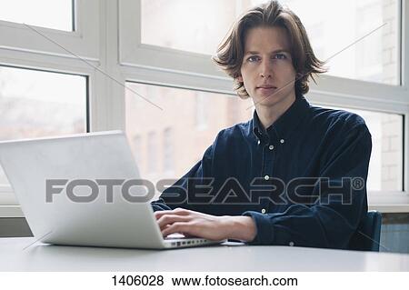 Portrait of confident young man using laptop at a desk View Large Photo Image Stock Photo - Portrait of confident young man using laptop at a desk. Fotosearch