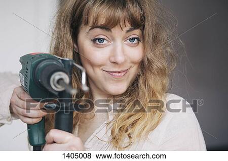 Stock Photo - Portrait of confident young woman holding power drill at home. Fotosearch