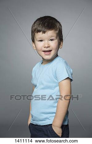 Picture - Portrait of happy boy standing with hands in pockets against gray background. Fotosearch