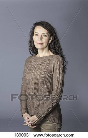 Stock Image - Portrait of happy mature woman standing hands clasped over gray background. Fotosearch