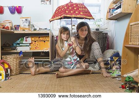 Portrait of happy mother with daughter holding umbrella while sitting on hardwood floor in domestic View Large Photo Image Stock Photo - Portrait of happy mother with daughter holding umbrella while sitting on hardwood floor in domestic . Fotosearch