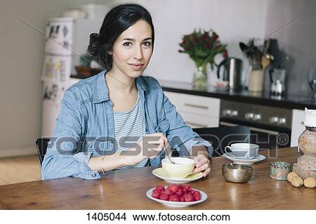 Picture - Portrait of happy young woman having coffee at table in kitchen. Fotosearch