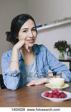 Portrait of happy young woman sitting at table in kitchen View Large Photo Image Stock Photo - Portrait of happy young woman sitting at table in kitchen. Fotosearch