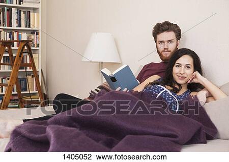 Stock Image - Portrait of happy young woman with man holding book in bed. Fotosearch