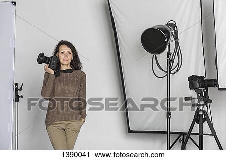 Stock Image - Portrait of mature female photographer with camera in photo studio. Fotosearch