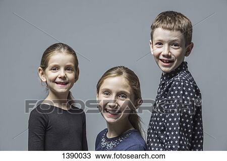 Stock Image - Portrait of smiling brother with sisters over gray background. Fotosearch