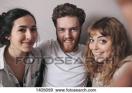 Stock Photo - Portrait of smiling young man with female friends spending leisure time at home. Fotosearch