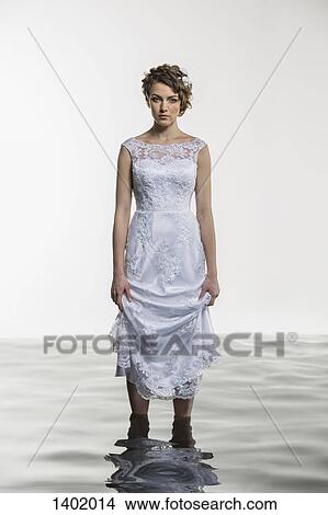 Portrait of young bride holding dress while standing in water against white background View Large Photo Image Picture - Portrait of young bride holding dress while standing in water against white background. Fotosearch