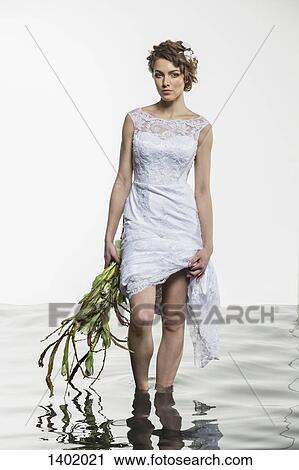 Portrait of young bride holding dress and wilted bouquet while standing in water against white backg View Large Photo Image Stock Image - Portrait of young bride holding dress and wilted bouquet while standing in water against white backg. Fotosearch