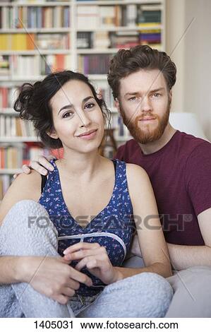Stock Image - Portrait of young woman with man relaxing at home. Fotosearch