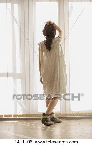 Stock Photograph - Rear view of woman looking through window at home. Fotosearch