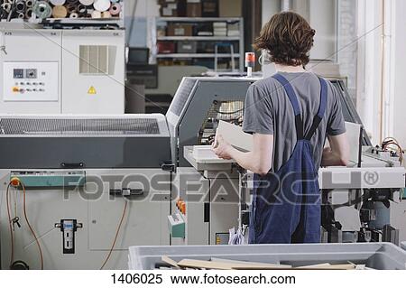 Stock Photography - Rear view of young male worker operating machine in factory. Fotosearch