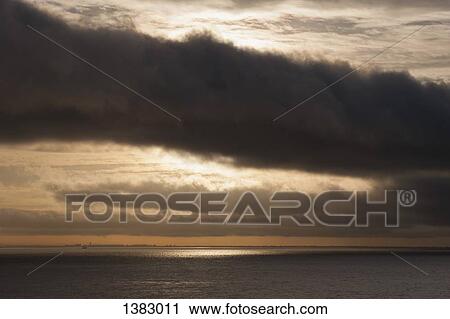 Stock Image - Scenic view of sea against cloudy sky during sunset. Fotosearch