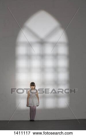 Stock Photo - Shadow of window falling on girl standing against white wall at home. Fotosearch