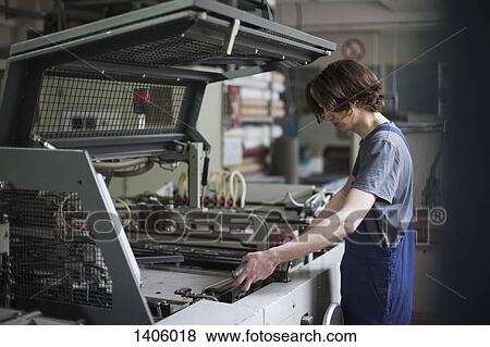 Stock Photo - Side view of young manual worker oiling machine in factory. Fotosearch