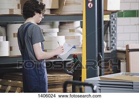 Picture - Side view of young worker writing on paper in warehouse. Fotosearch
