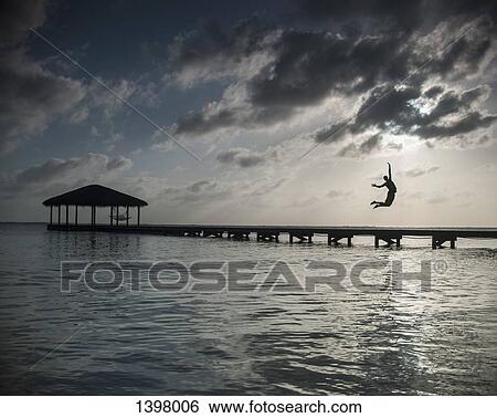 Silhouette person jumping into sea against cloudy sky at dusk View Large Photo Image Stock Photograph - Silhouette person jumping into sea against cloudy sky at dusk. Fotosearch