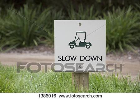 Stock Photograph - Slow down warning sign on field by dirt road. Fotosearch