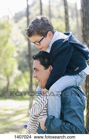Picture - Smiling man carrying son on shoulders in forest. Fotosearch