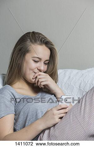 Smiling teenage girl using smart phone on sofa at home View Large Photo Image Stock Image - Smiling teenage girl using smart phone on sofa at home. Fotosearch