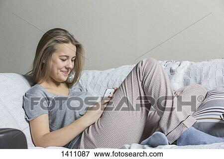 Stock Photo - Smiling teenage girl using smart phone on sofa at home. Fotosearch