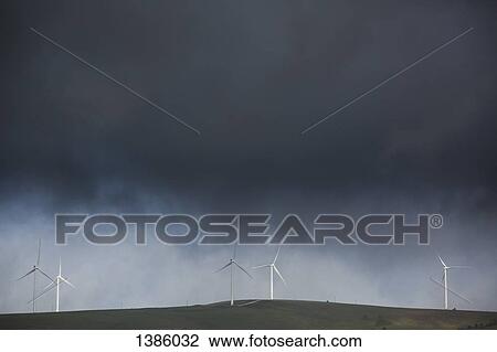 Stock Image - Stormy clouds over wind turbines on agricultural field. Fotosearch