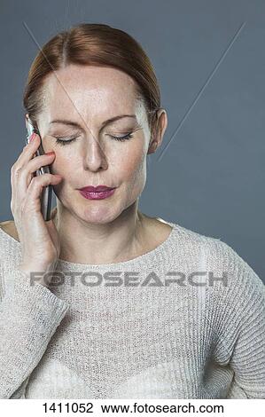 Stressed mature woman using mobile phone against gray background View Large Photo Image Stock Image - Stressed mature woman using mobile phone against gray background. Fotosearch