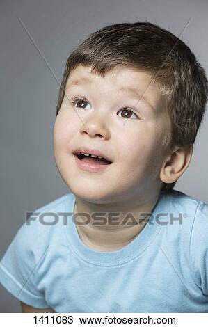 Stock Image - Surprised boy looking up against gray background. Fotosearch