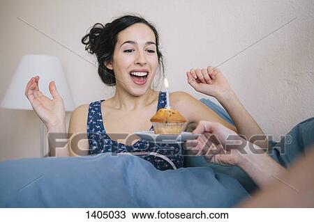 Surprised young woman blowing out candle on cupcake held by man at home View Large Photo Image Stock Image - Surprised young woman blowing out candle on cupcake held by man at home. Fotosearch