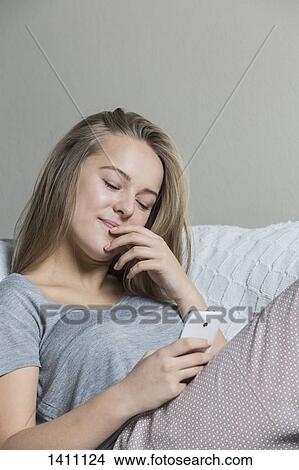 Picture - Teenage girl using smart phone on sofa at home. Fotosearch