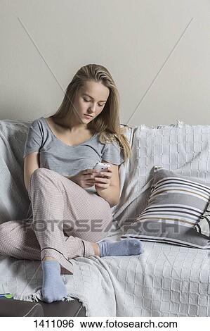 Teenage girl using smart phone on sofa at home View Large Photo Image Stock Photograph - Teenage girl using smart phone on sofa at home. Fotosearch