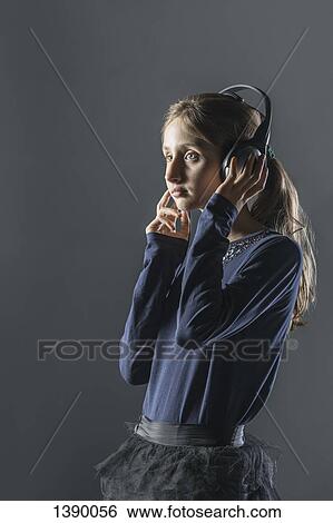 Thoughtful girl listening music through headphones over gray background View Large Photo Image Stock Photograph - Thoughtful girl listening music through headphones over gray background. Fotosearch