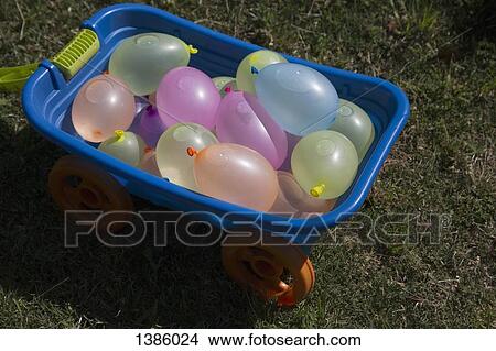 Picture - Toy wheelbarrow filled with water balloons at yard. Fotosearch