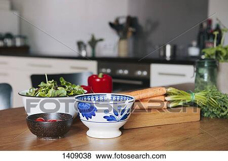Stock Photo - Vegetables and bowls on wooden table in kitchen. Fotosearch