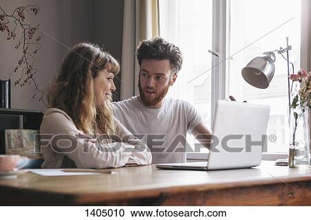 Stock Image - Young couple having discussion with laptop on table at home. Fotosearch
