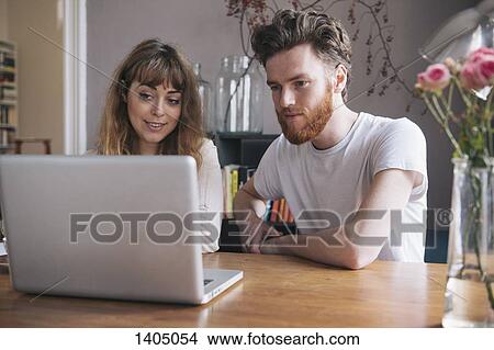 Young couple looking at laptop on table View Large Photo Image Picture - Young couple looking at laptop on table. Fotosearch