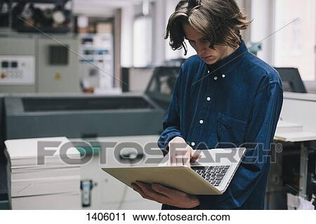 Stock Image - Young male technician using laptop in factory. Fotosearch