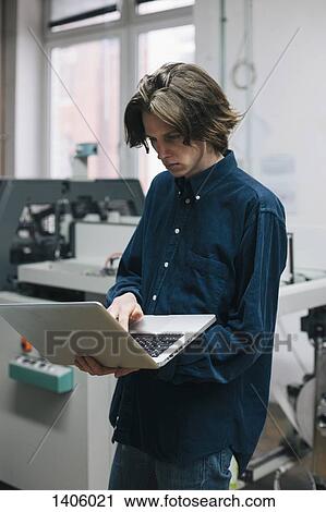 Stock Image - Young male technician using laptop in factory. Fotosearch