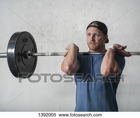 Stock Photography - Young man lifting barbell in gym. Fotosearch