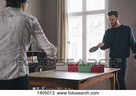 Stock Image - Young man playing table tennis with woman at home. Fotosearch