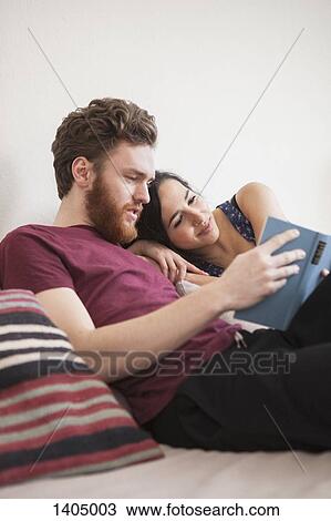 Stock Image - Young man reading book for woman in bed. Fotosearch