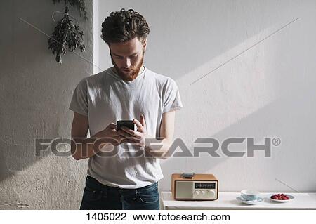 Young man using mobile phone at home View Large Photo Image Stock Image - Young man using mobile phone at home. Fotosearch