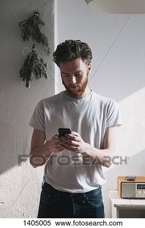 Young man using mobile phone at home View Large Photo Image Stock Photography - Young man using mobile phone at home. Fotosearch