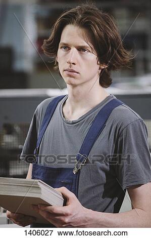 Stock Photo - Young manual worker holding cardboard sheets in factory. Fotosearch