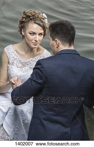 Stock Photo - Young newlywed couple holding hands at lakeshore. Fotosearch