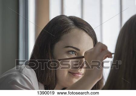 Stock Photo - Young woman applying make-up to friend. Fotosearch