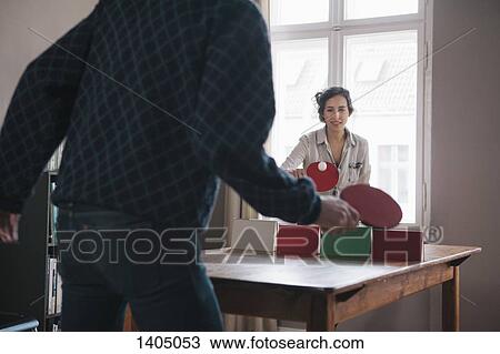 Stock Image - Young woman playing table tennis with man at home. Fotosearch