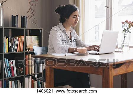 Stock Image - Young woman using laptop at table. Fotosearch