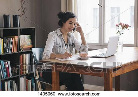 Young woman using mobile phone with laptop on table at home View Large Photo Image Stock Image - Young woman using mobile phone with laptop on table at home. Fotosearch